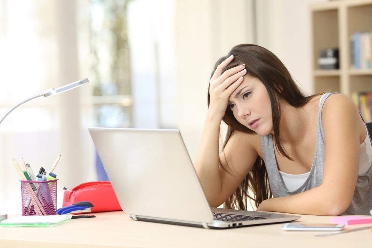a teenage girl looks frustrated sitting at her laptop