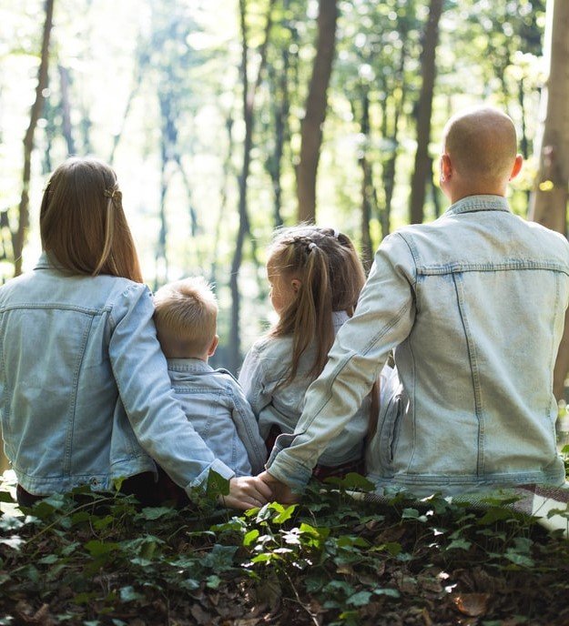 family with parents and two small children sitting together in the woods