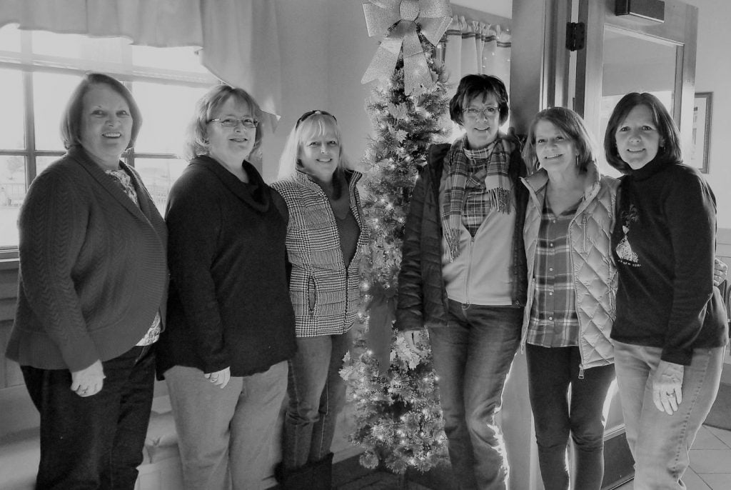 six female friends standing around a christmas tree