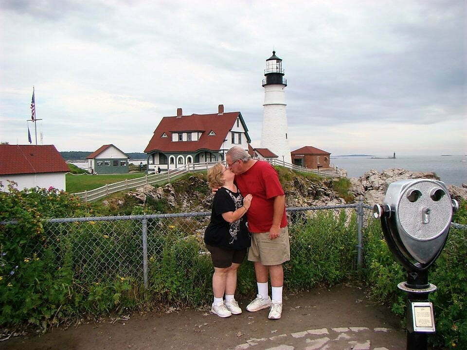 man and woman kissing with portland light house in the background