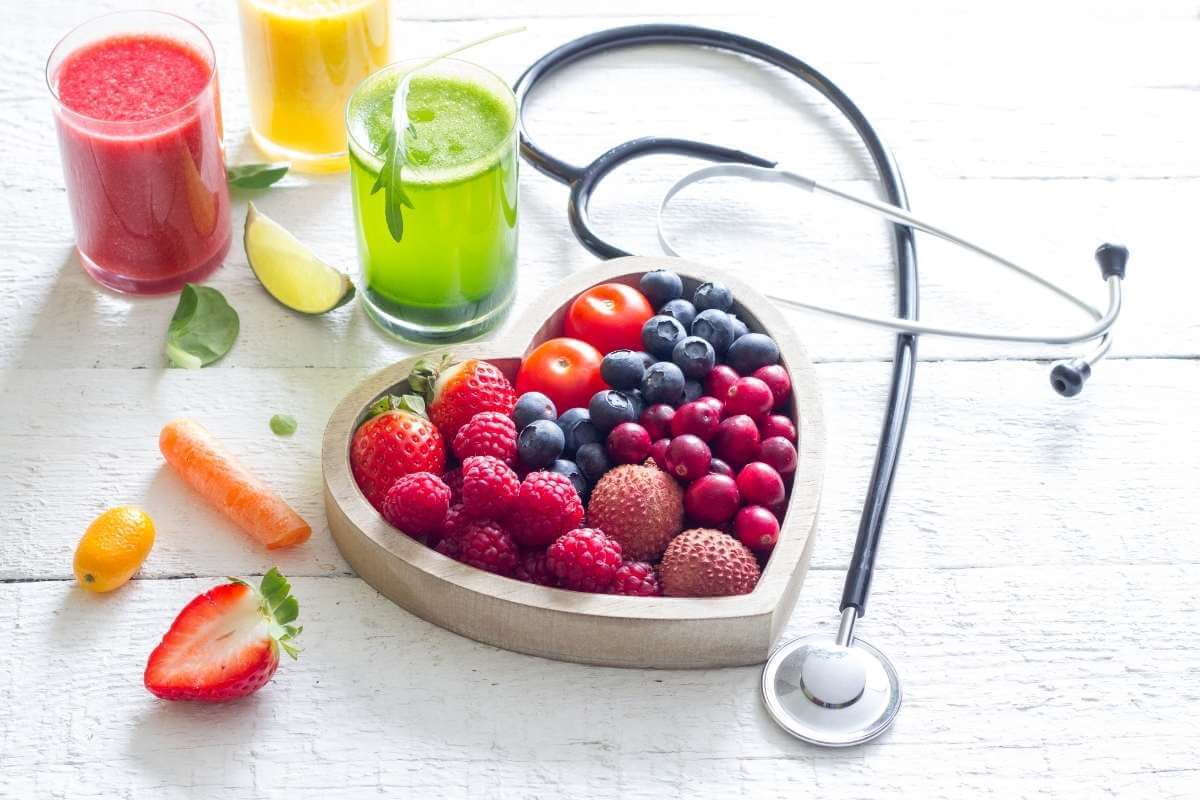 heart shaped dish with fresh fruits 3 glasses of juices and a stethoscope