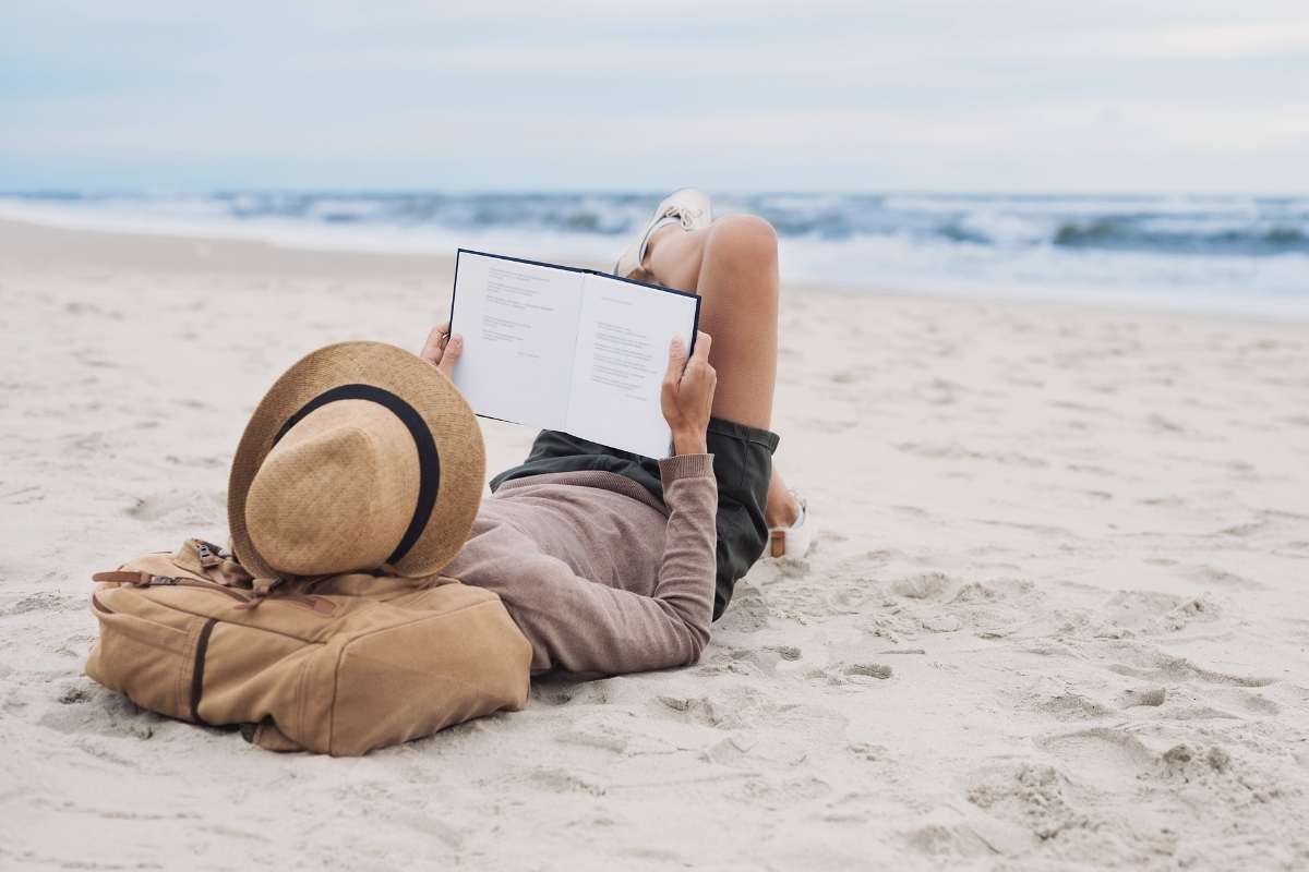 women laying on beach reading a book peacefully showing habits to  improve mental health