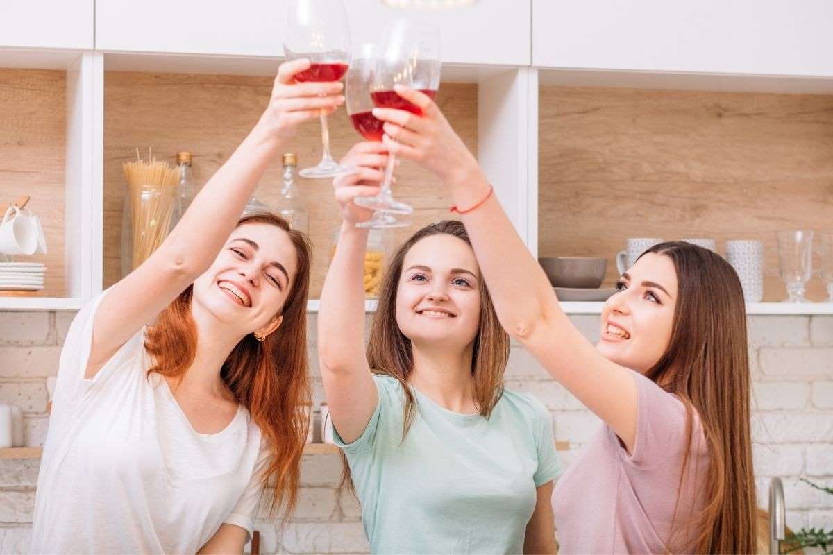 three women celebrating each other by toasting with glasses of red wine because they are hard working women