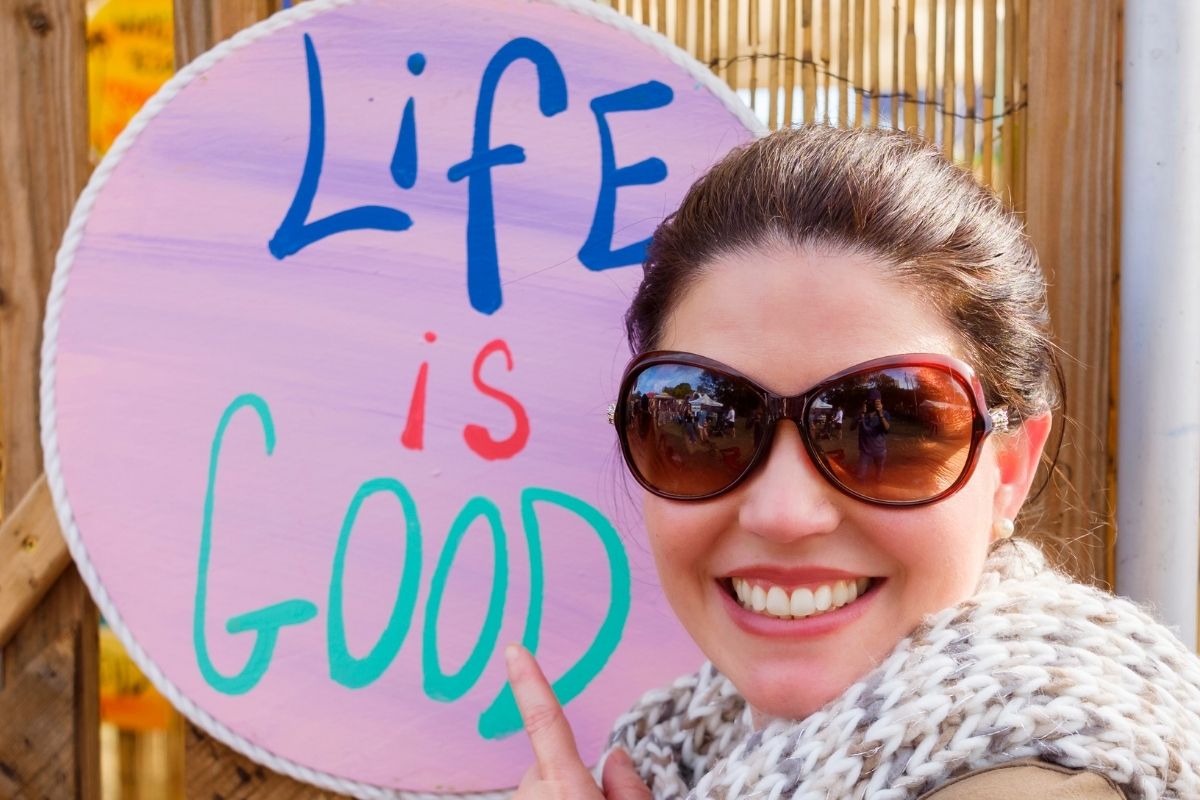 smiling woman pointing to a life is good sign showing she is happy