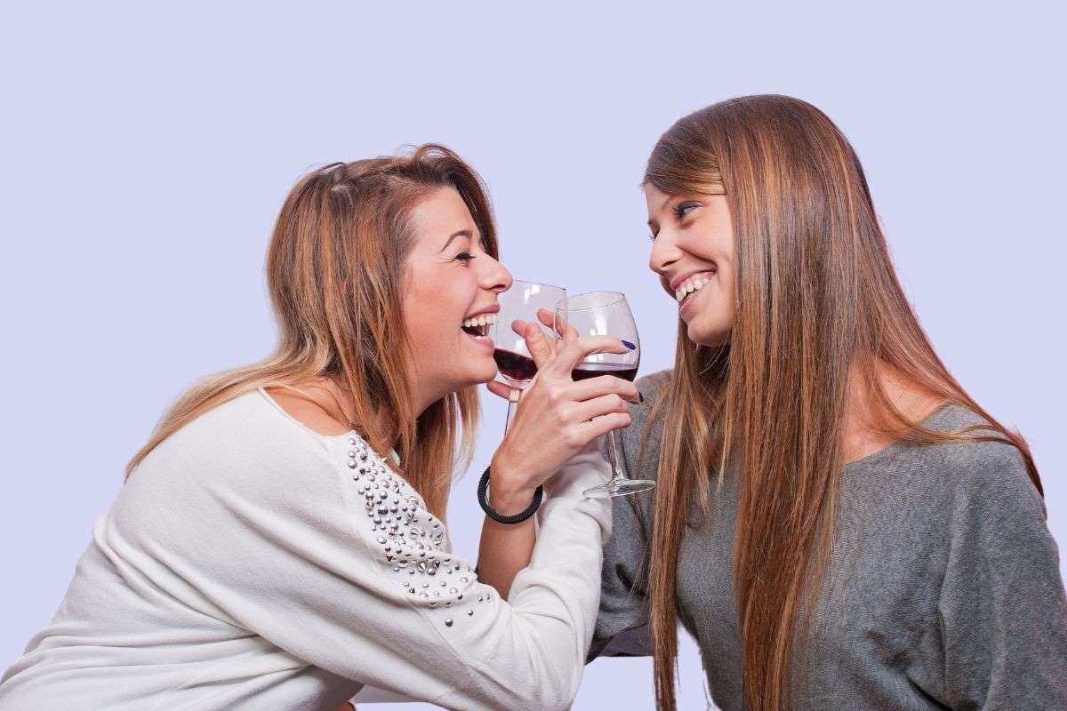 two women smiling with interlocking arms sipping on wine