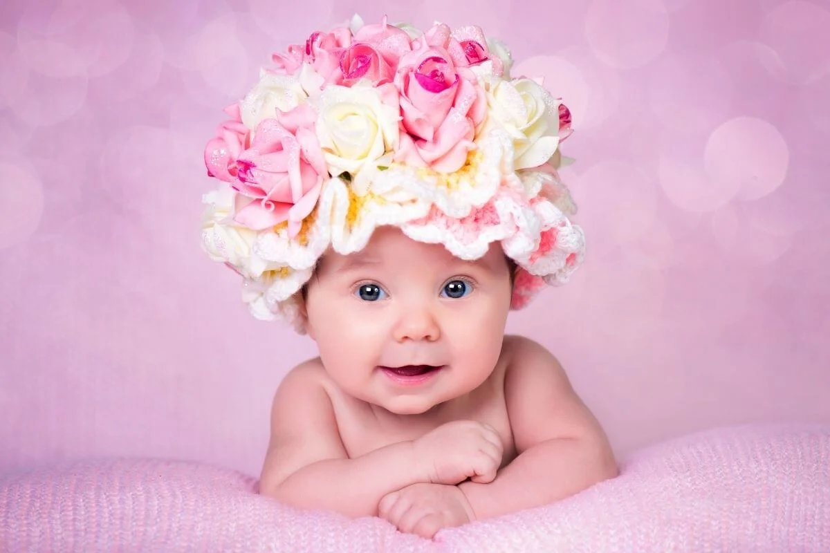 happy baby girl with big pink and white hat made of roses and crochet on a pink background and blanket