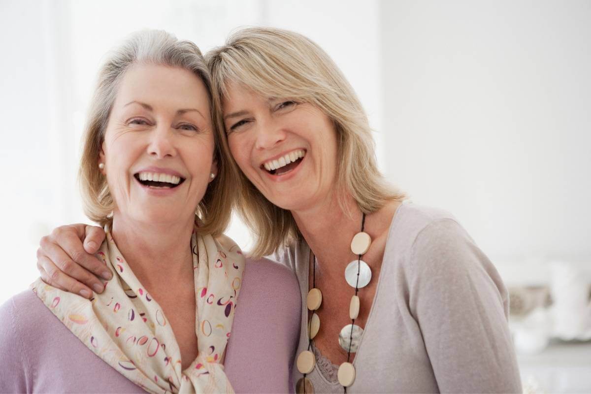 two older women stand head to head hugging with big smiles on their faces