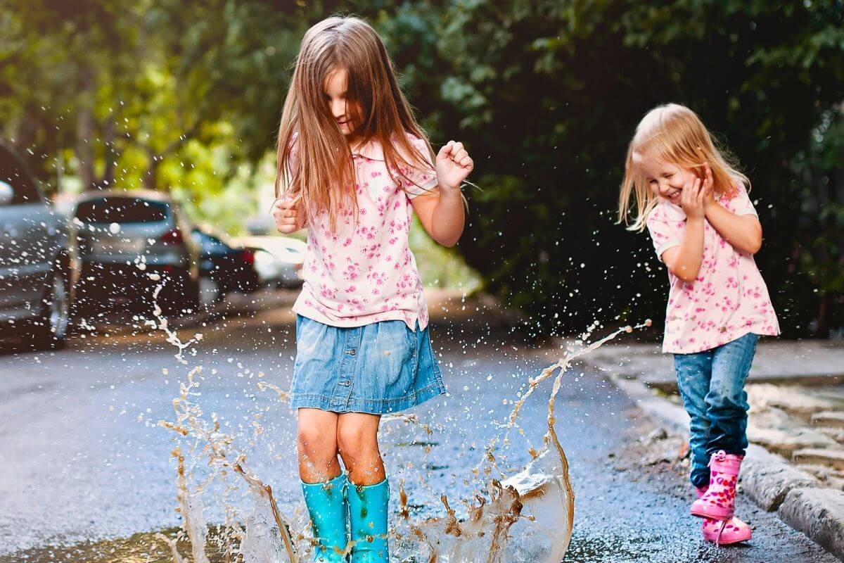 two little girl play in a puddle of water laughing and having lots of fun as they celebrate life every day