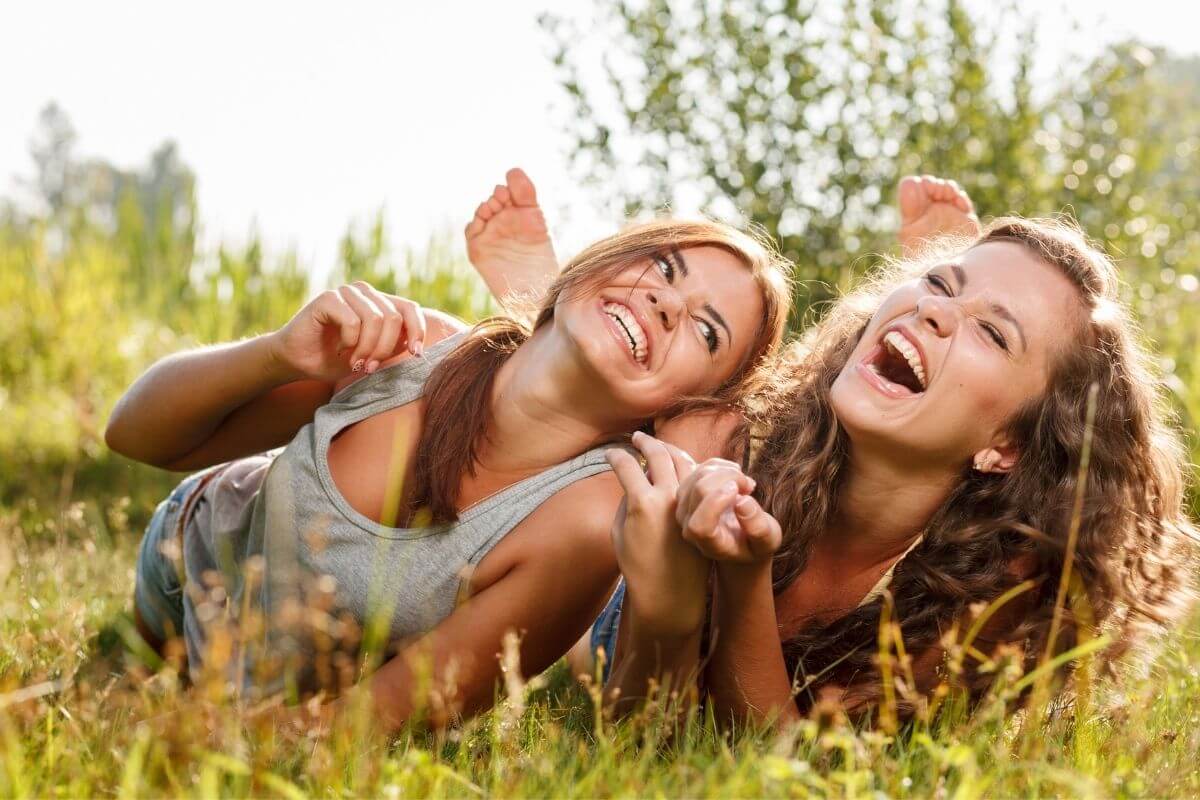 two happy young ladies lay in the grass socializing and laughing