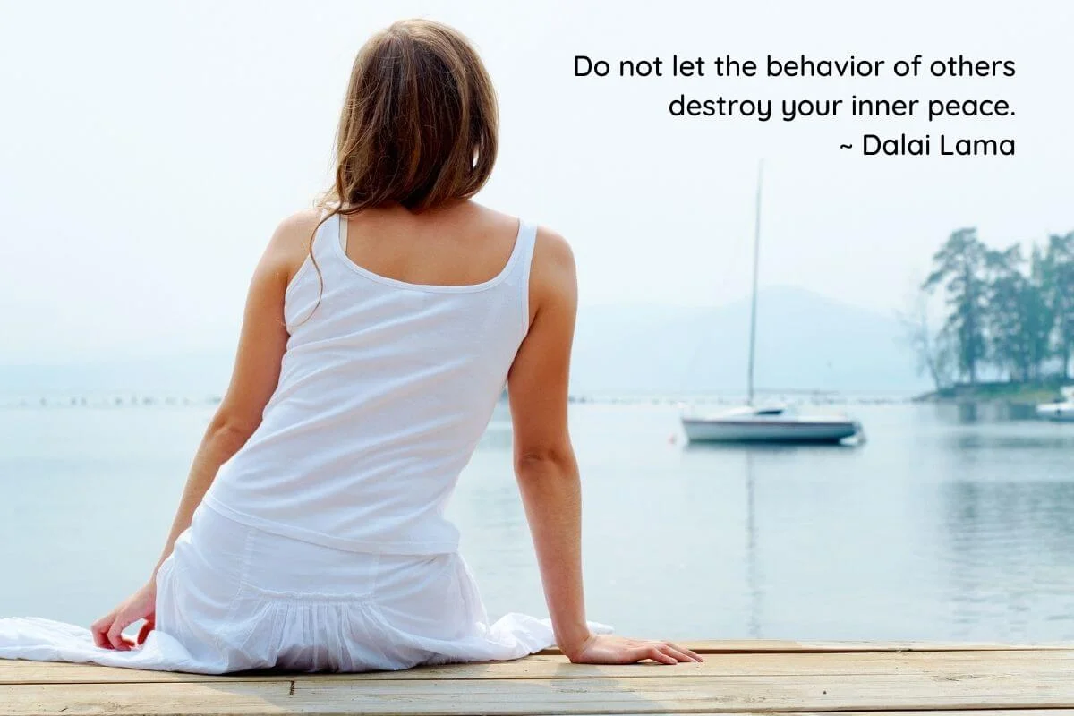 young woman sitting on a pier looking out onto a lake with a boat and a Dalai Lama quote about inner peace