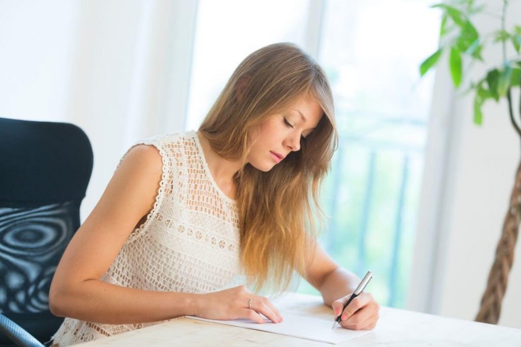 a woman sits at a desk and writes a letter to her younger self