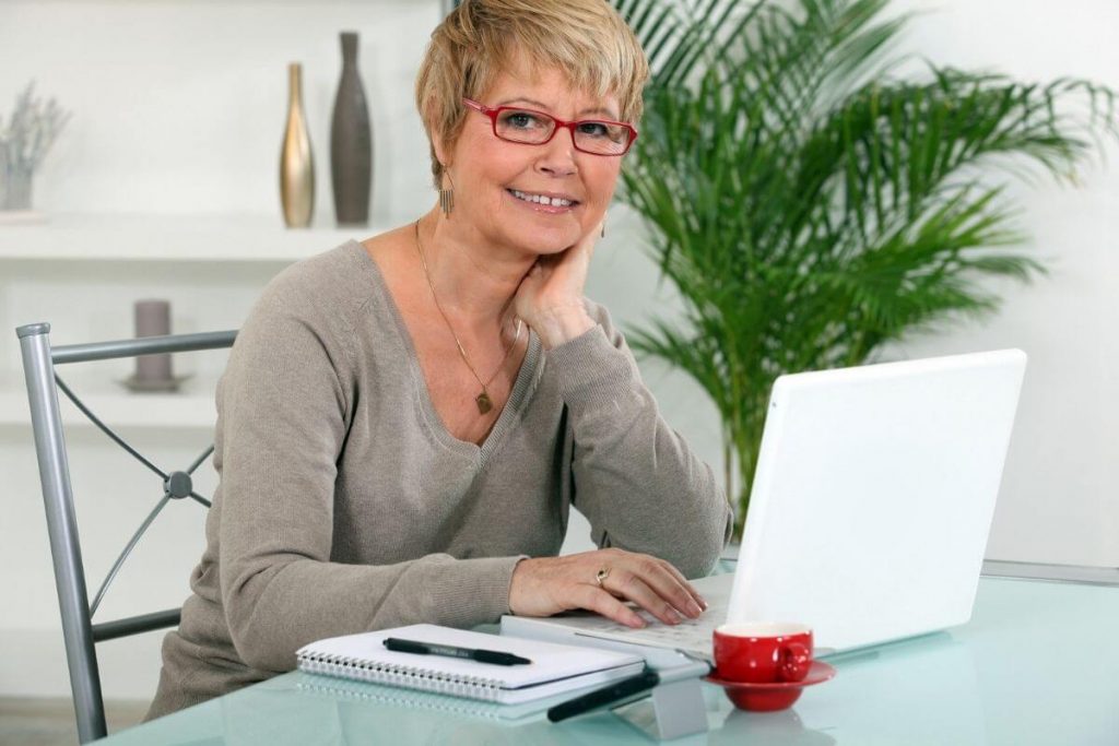 smiling lady uses a laptop and paper to write a letter to her younger self