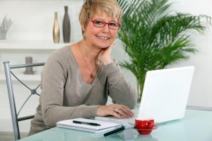 smiling lady uses a laptop and paper to write a letter to her younger self