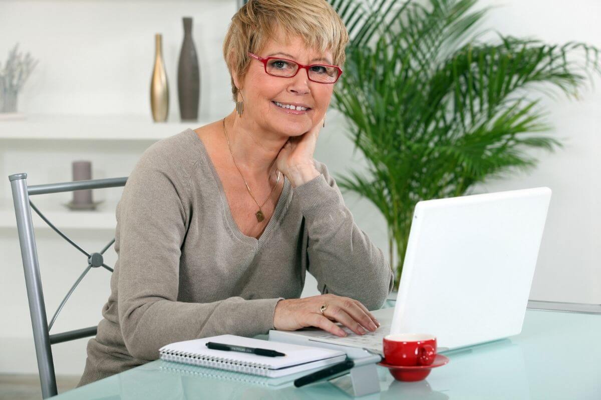 smiling lady uses a laptop and paper to write a letter to her younger self