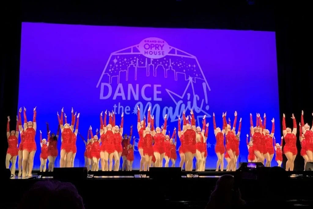 dancers in red costumes on the Grand Ole Opry Stage with a Dance the Magic backdrop