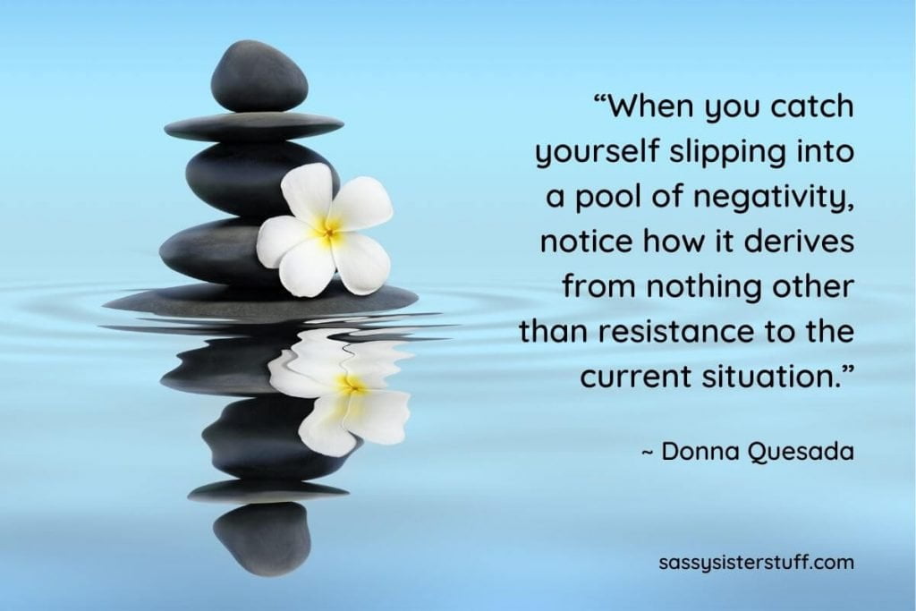 five black rocks stacked on top of each other in a blue pool of water with a white lily and a quote about positivity