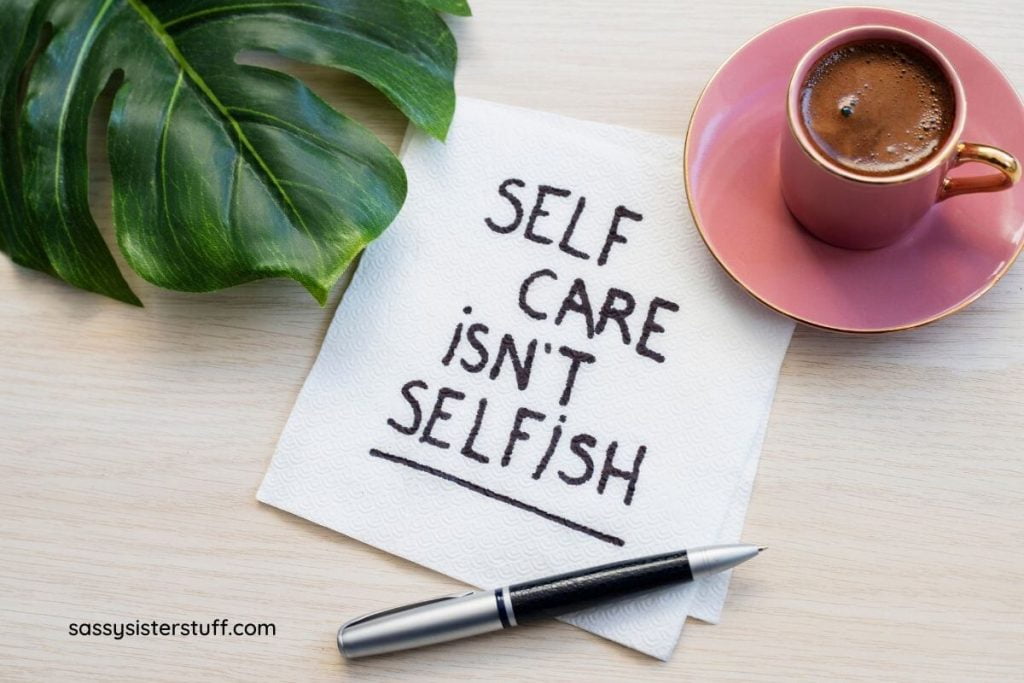a napkin says self care isn't selfish and a mug of hot chocolate and a large leaf