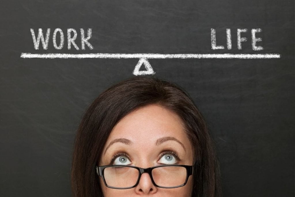 the top of a woman's head with her eyes rolled upwards looking at a balance beam drawn over head on a blackboard showing work life balance