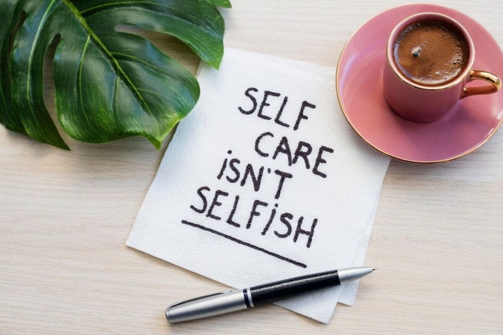 a green leaf a pink cup of hot chocolate with a napkin that says self care isn't selfish
