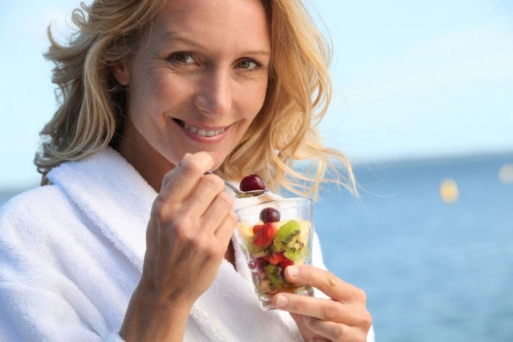 a middle aged blonde woman eats a healthy cup of fruit on self care Sunday