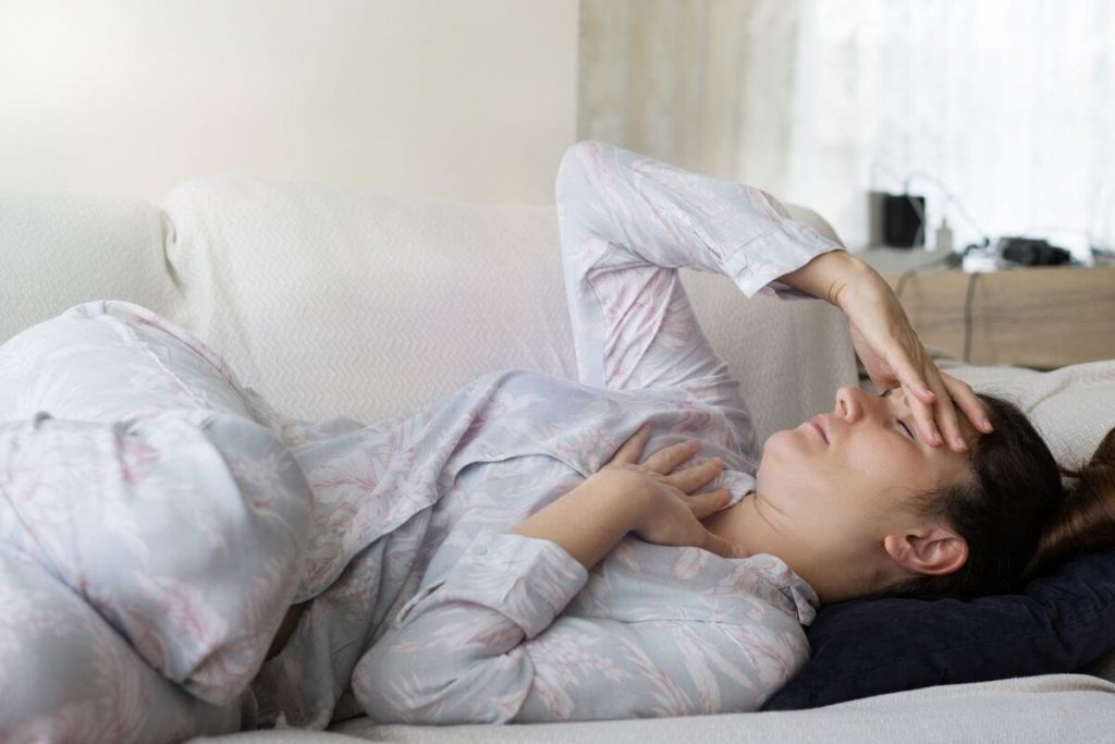a woman with chronic pain lays on her sofa hold her head and chest