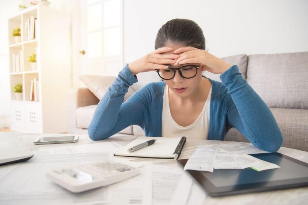 a young woman studies her financial status and holds her head in frustration