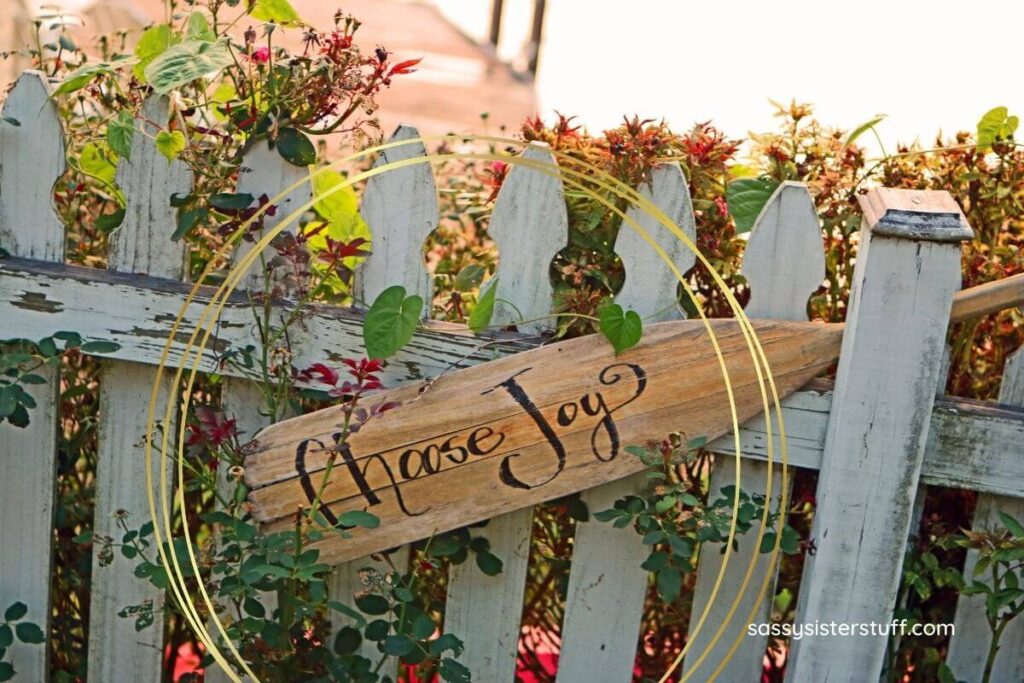a gray wooden fence with flowers winding through it and a brown wooden sign that says choose joy