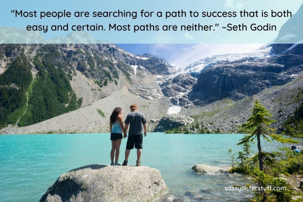 a young couple stand on a large rock in a blue lake with rocky mountains in the background and a find your path quote