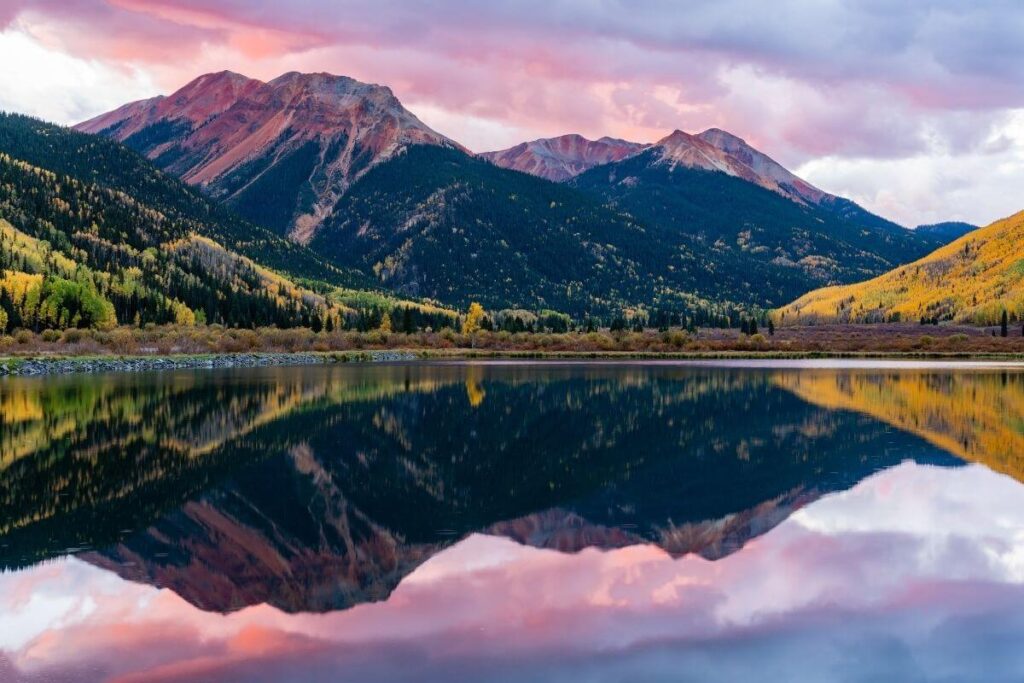 a beautiful mountain landscape photo with a lake in front and lots of colors like blue purple yellow pink green white