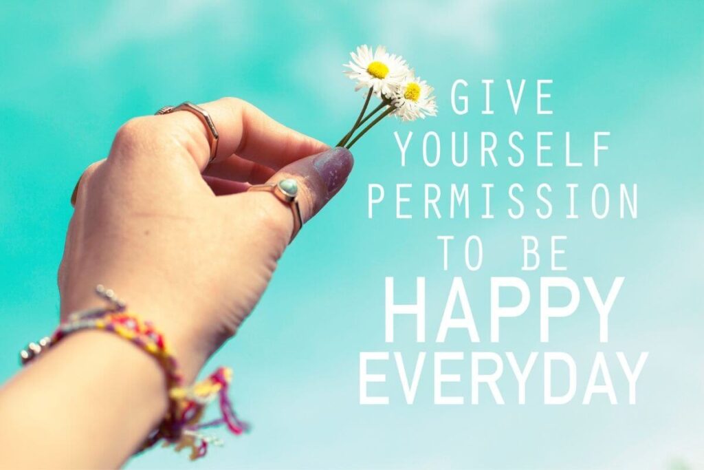 be happy everyday quote on a mint background and a female hand holding two daisies
