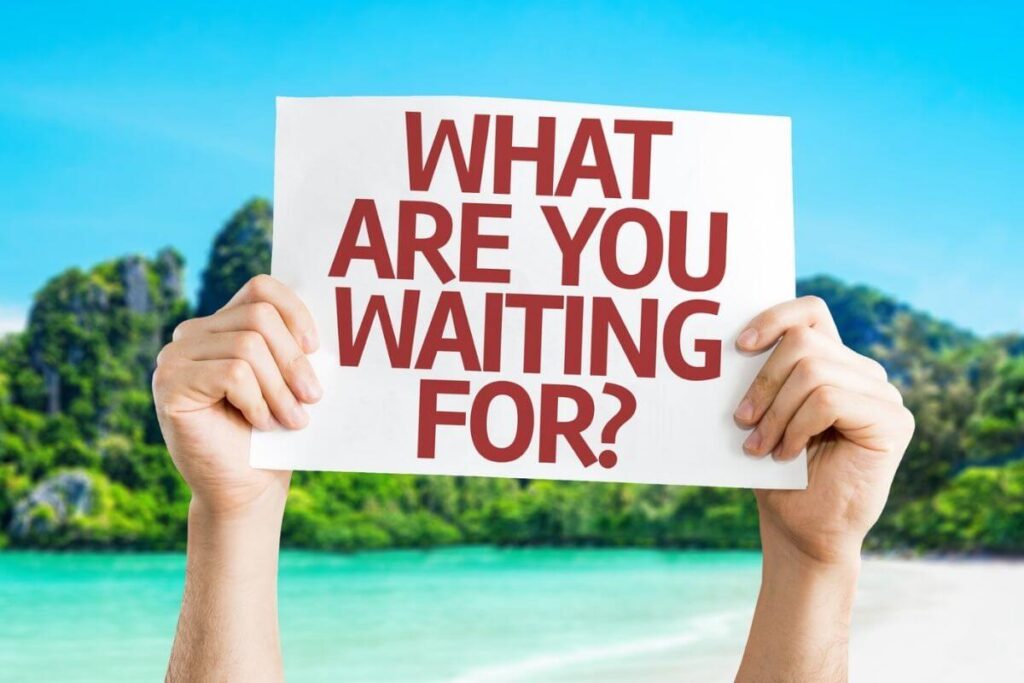 female hands holding up a sign that says what are you waiting for? in front of a tropical island of tress and turquoise water