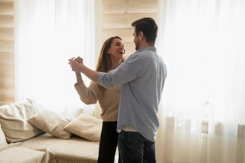 a young happy couple dances in their living room as part of the commitment to slow living
