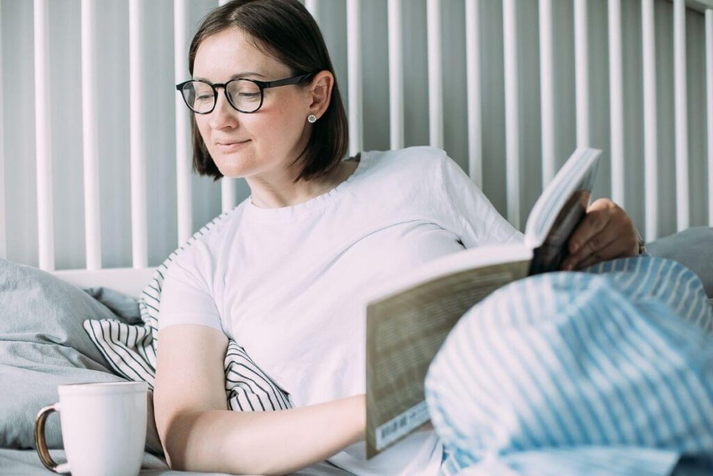 a woman relaxes in bed with a cup of coffee and a book as she lives a slow and cozy life