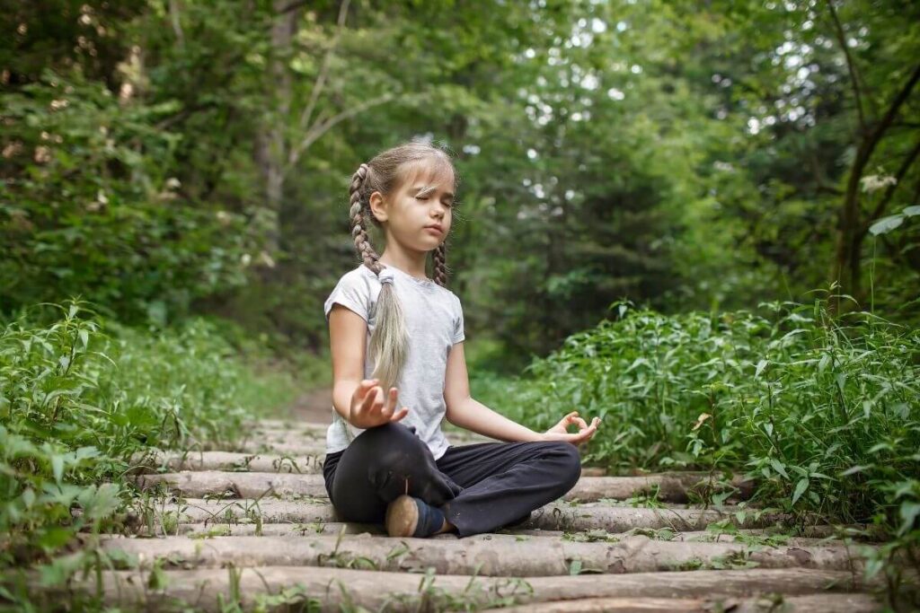 a little girl does yoga on a wooden path in the green forest