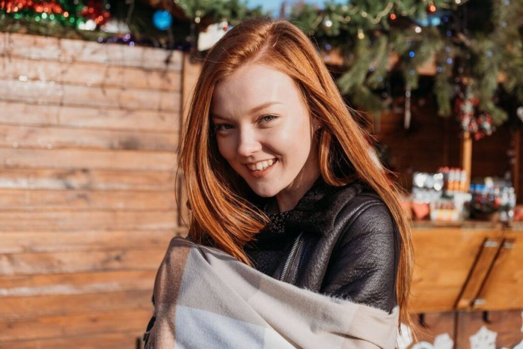 a young red haired woman smiles at the camera in an outdoor holiday setting where she is enjoying a slow living lifestyle