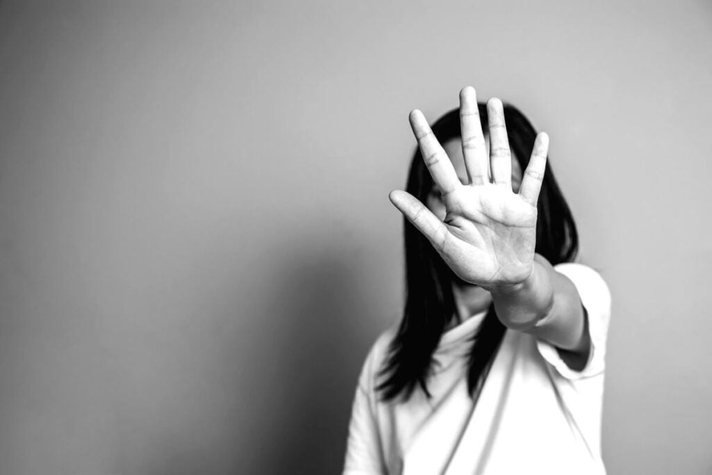 woman with dark hair holds her hand up in front of her face to indicate a BACK OFF message to an adult bully