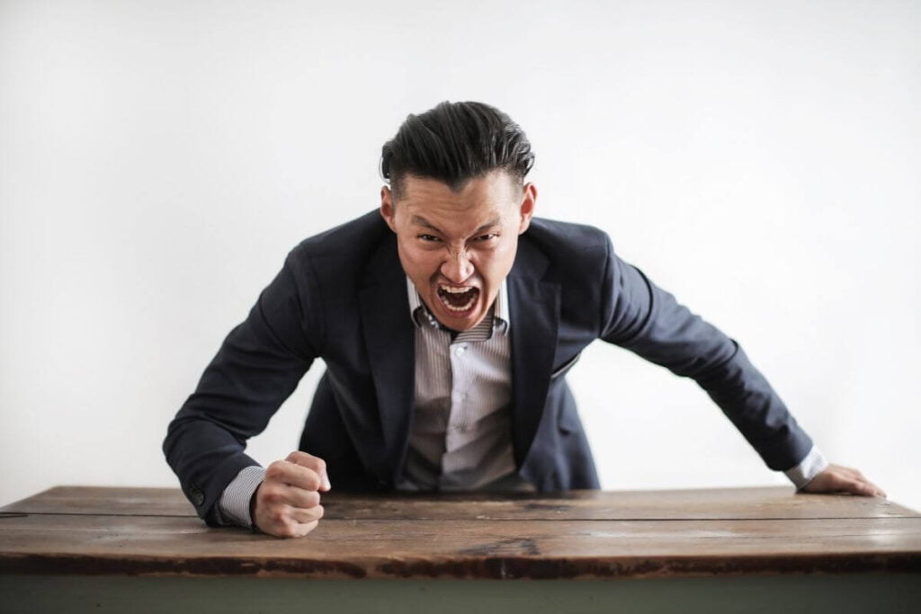 angry and aggressive adult bully bangs his fist on a table and screams in a terrifying manner