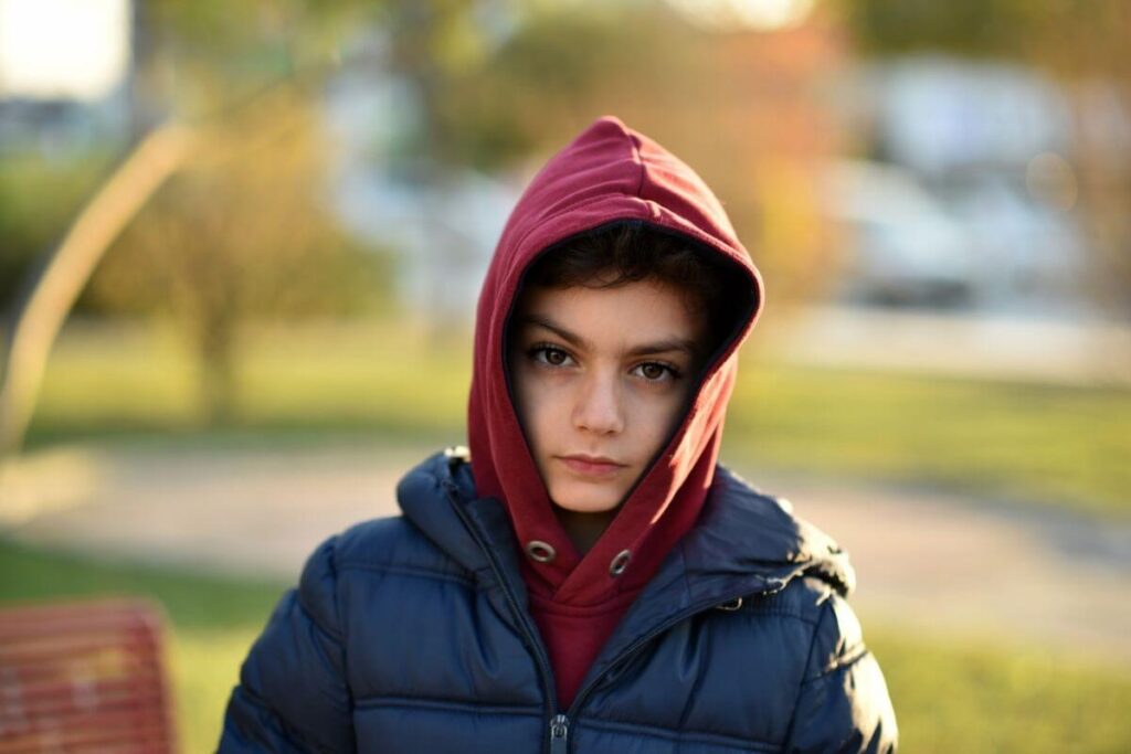 young teen boy wears a hoodie over his head and looks sad as he walks home from school because his schools anti-bullying policies are not working and he sees his friends bullying other students