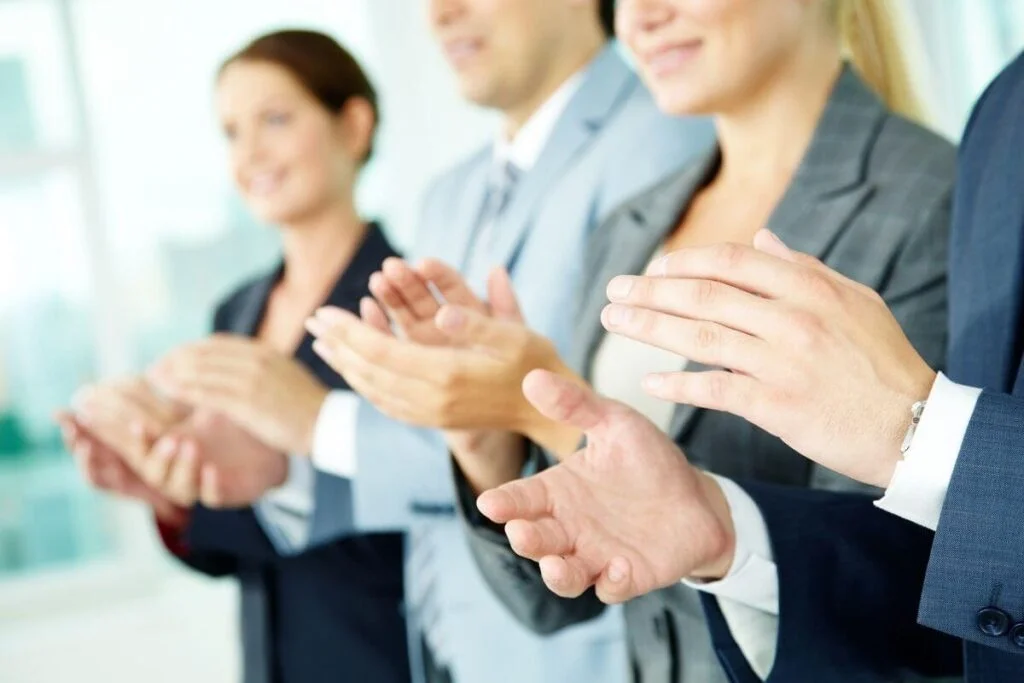 four business men and women in suits are clapping for someone's success