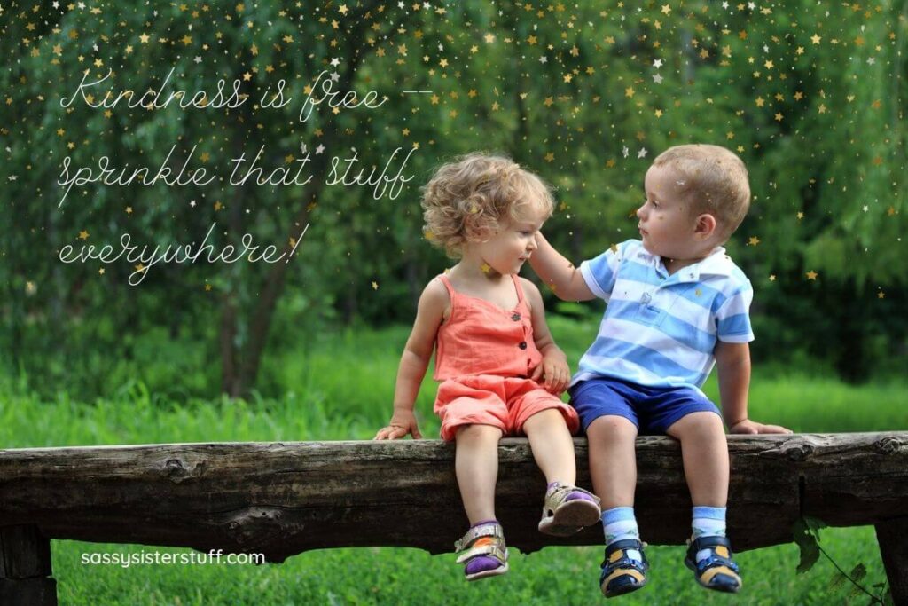 a little boy toddle and girl toddler sit on a log bench in the woods and he reach gently to play with her curly hair as they enjoy each others kindness plus a kindness quote in the corner