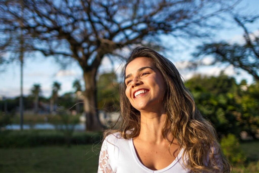 a confident pretty young woman stands outside in a park and smile happily about boss babe quotes that have empowered her to be her own boss