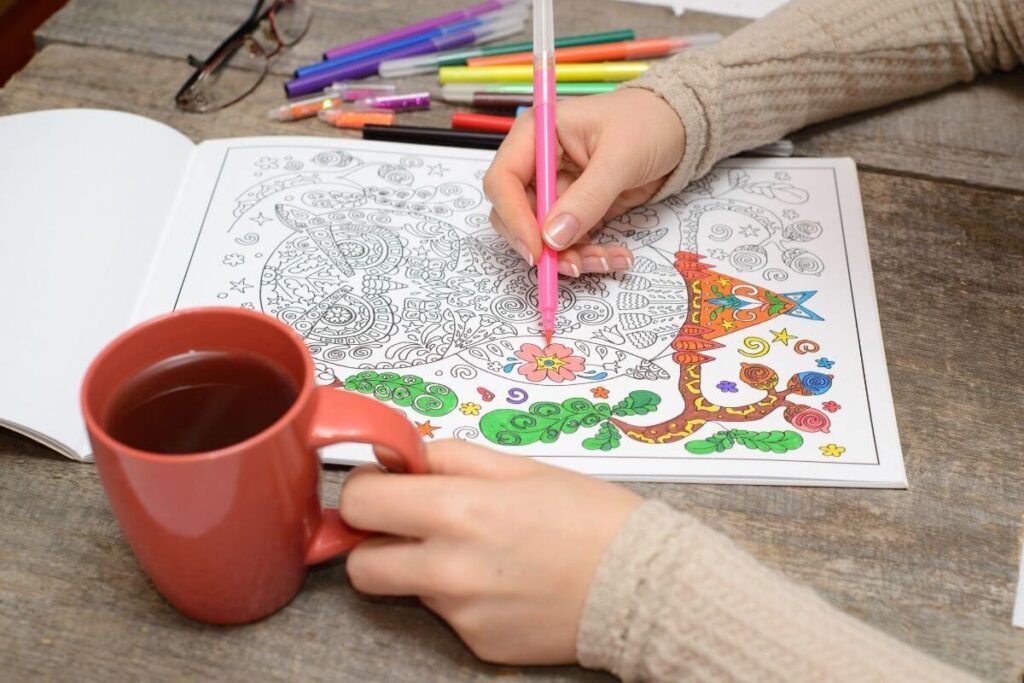 top view of woman using colored pencils on calming coloring pages as she relaxes with a cup of coffee