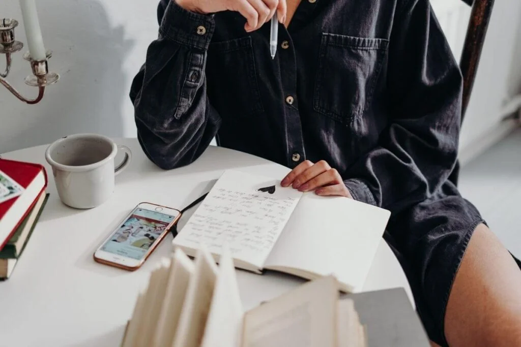 top view of a woman sitting at a small table writing in a journal relaxing with her coffee