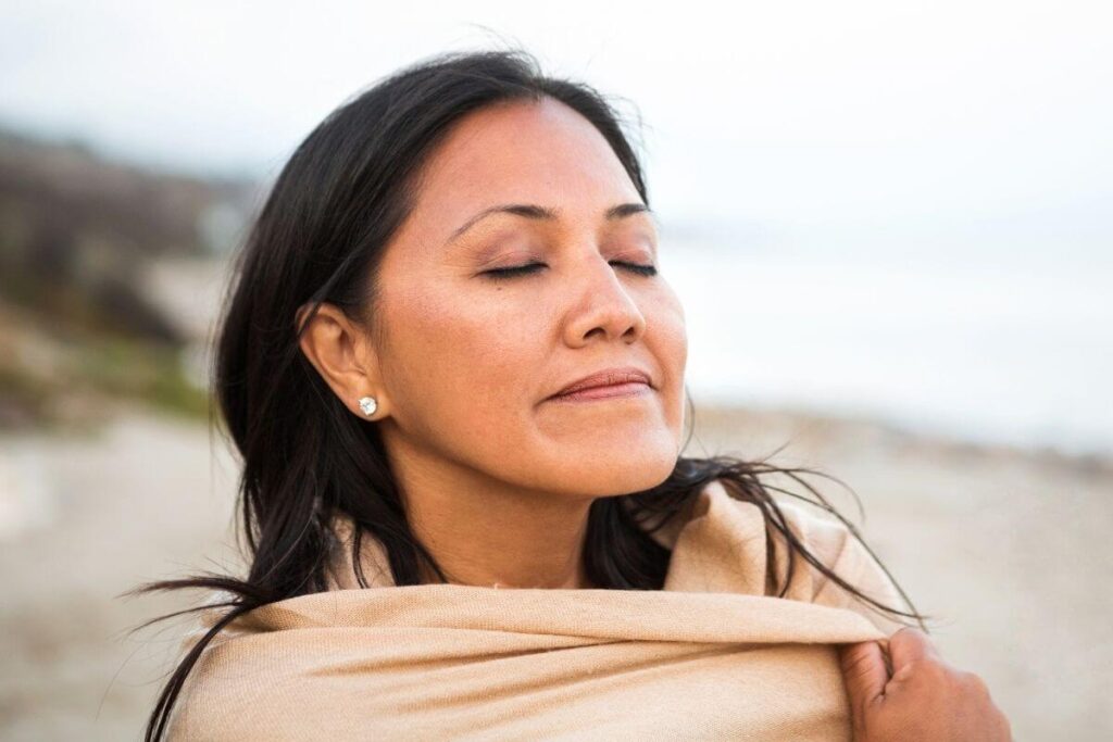 a close-up of a woman wrapped in a soft shawl walking along the beach feeling I just want a peaceful life