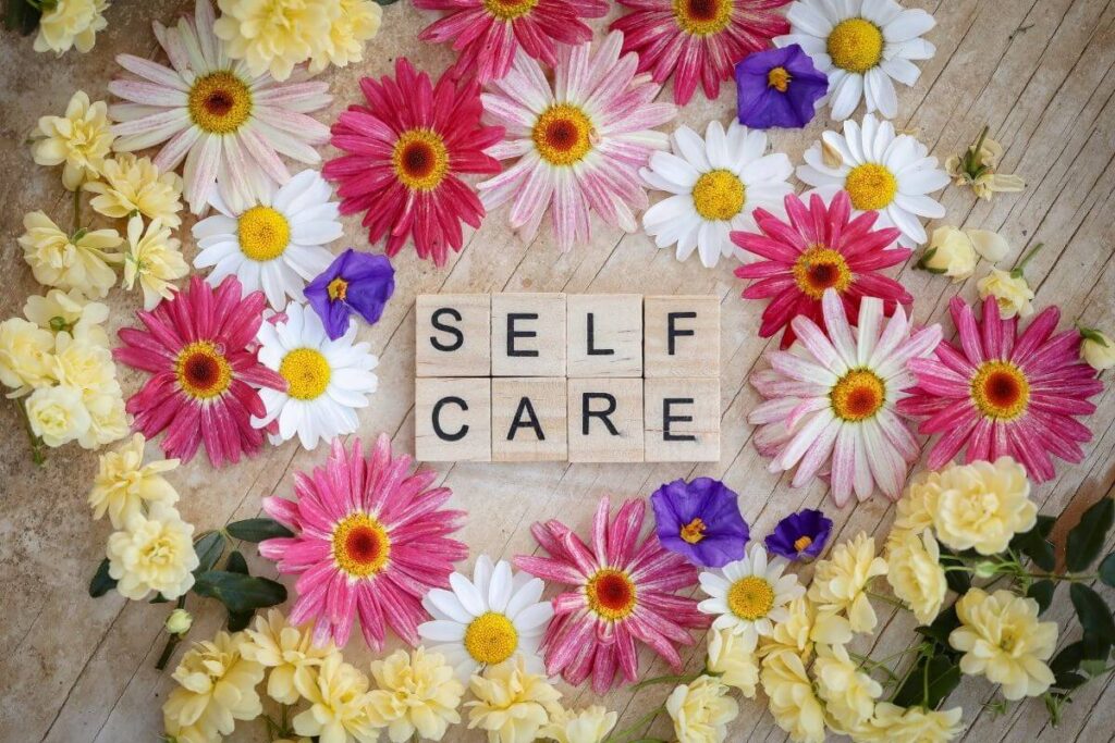 beautiful spring flowers lay on a rustic wooden table surrounding wooden tiles that say self care