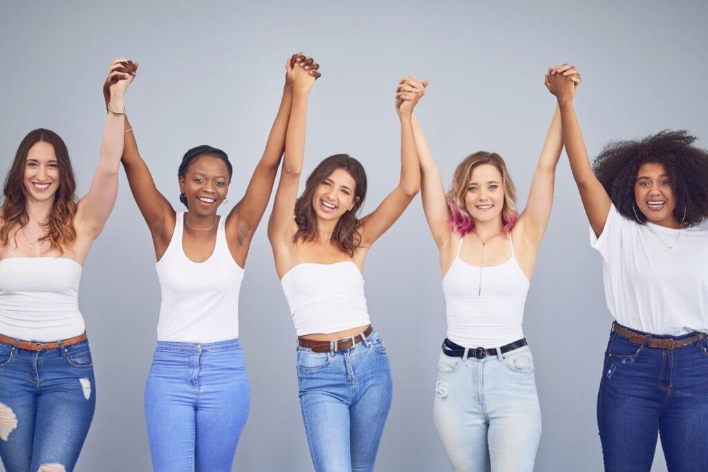 five ladies of varying shapes sizes and colors stand together in unity holding hands in the air smiling as they reaffirm key personal development topics that they focus on to help make their lives great