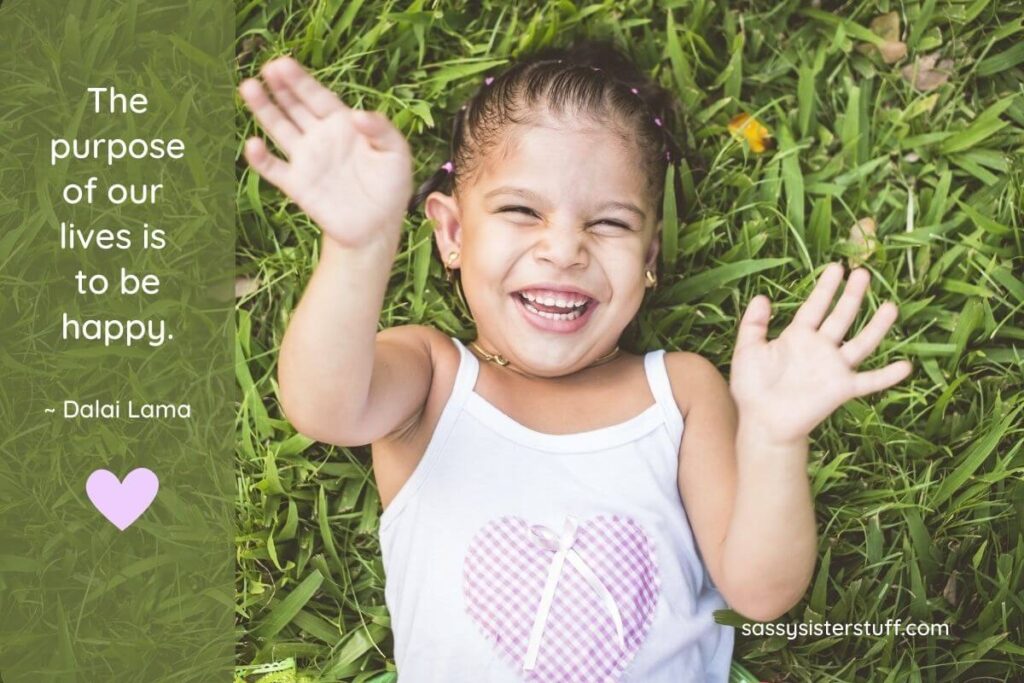 a top view of a precious little girl laying in the grass laughing aloud and a quote about happiness from dalai lama