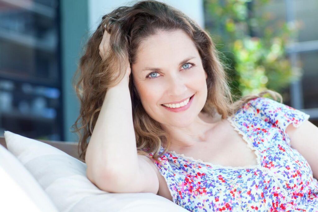 middle ages brown hair woman smiles at the camera as she relaxes on outdoor furniture in the sunlight and shows how to carry yourself with confidence