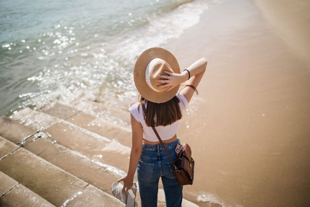 a young woman stands on the edge of the shoreline looking out into the ocean showing signs of good personal growth because she enjoys being alone now