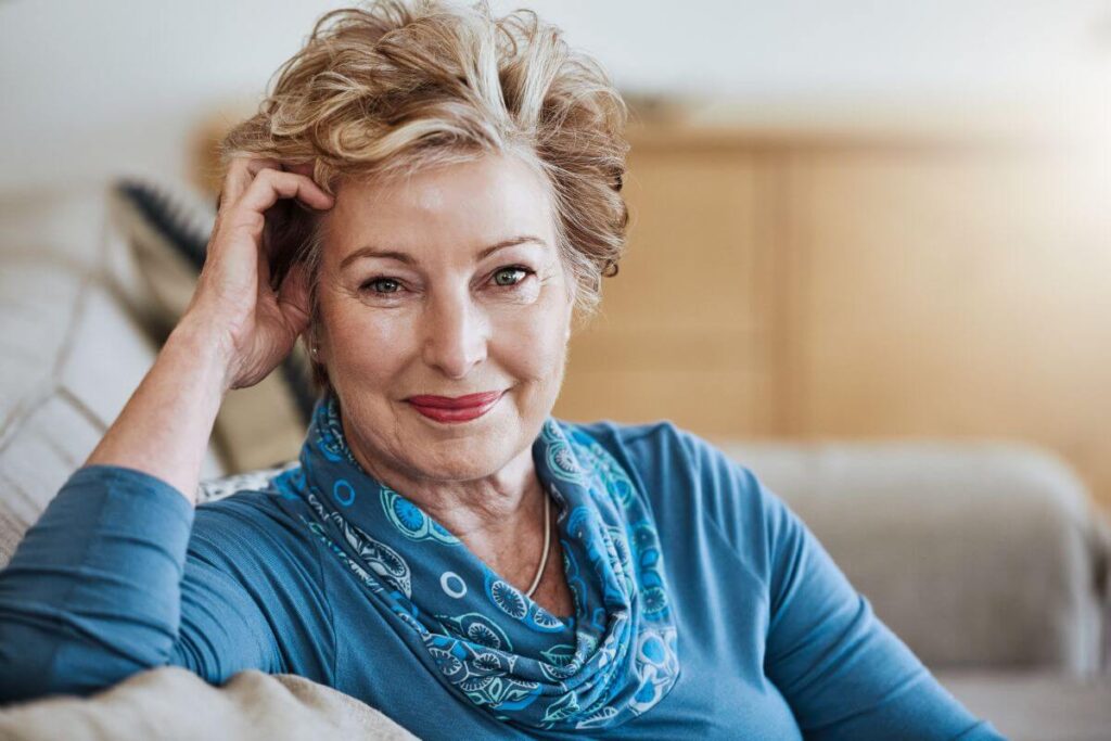 a happy fulfilled middle-aged woman with short blonde hair sits on a sofa smiling at the camera pondering the question what is wellness and why is it important